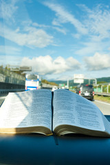 Open Holy Bible inside car on Tomei Expressway, Japan. Background with beautiful blue sky and white clouds. Vertical shot.
