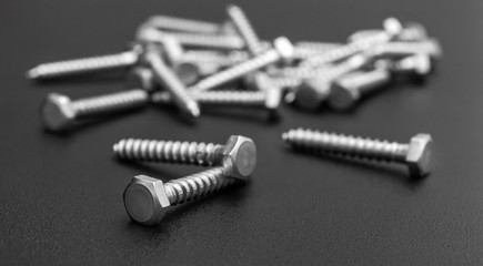Heap of metal hex screws on black.