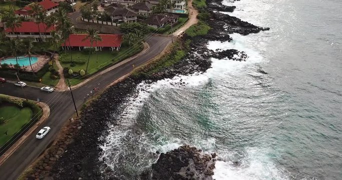 Drone tracking white car and beach front of Hawaii town of Poipu in Kauai with pool and ocean