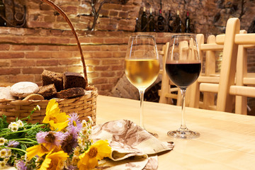 Still life with two glasses with red and white wine on wooden table in the old vintage wine cellar from red brick