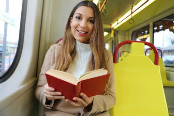 Beautiful young woman sitting in tram caught and surprised at reading her book looks at camera.