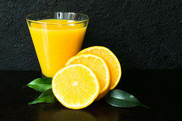 Glass of orange and slices of orange on a black background.