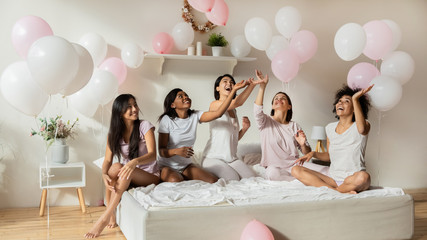 Beautiful multiethnic ladies having fun with pink balloons in bedroom