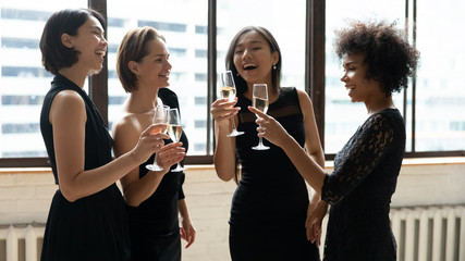 Stylish diverse ladies wear dresses drinking champagne celebrating birthday party