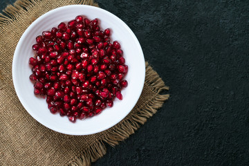 Pomegranate seeds served in a white plate on a black background. Flat lay. Copy space.