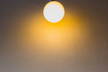 Yellow light bulb is hanging on white background.