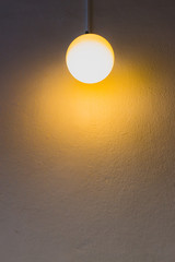 Yellow light bulb is hanging on white background.