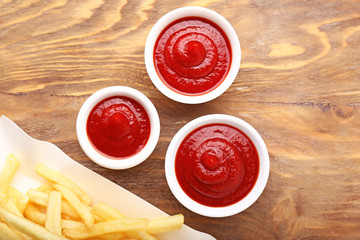 Tasty french fries and tomato sauce on wooden background