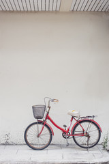 red bicycle with basket in front of the white wall, background