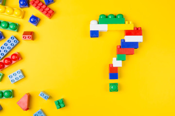 Details of a children's toy constructor folded as a question mark on a yellow background. Creative and educational concept.