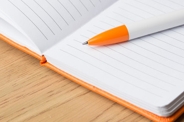 An orange ballpoint pen lies on the blank pages of an open notebook for writing
