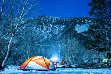 Illuminated Tent in Snow with Mountains and Stars