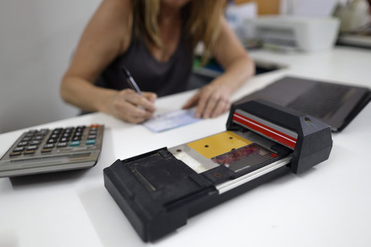 Clear image of old credit card imprinter machine on the white table with defocused female wrettening, signature on imprint paper work background