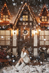Beautiful model girl with perfect body in Christmas rustic interior decorated for New year with artificial snow. Young woman posing in winter exterior of a country house with Christmas decorations.