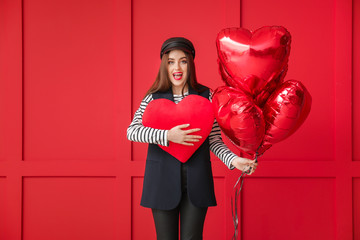 Beautiful young woman with big red heart and balloons on color background. Valentine's Day celebration