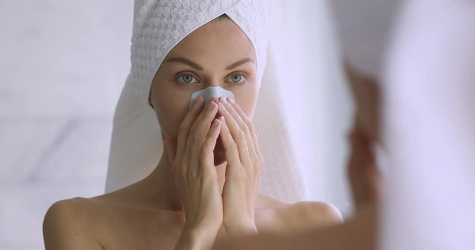 Smiling woman apply nose strip cleansing pores looking in mirror