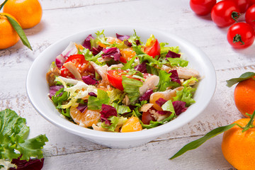  Salad with chicken, tangerines and vegetables in a bowl on an old rustic wooden table