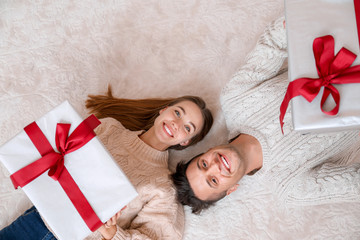 Happy young couple with Christmas gifts lying on floor, top view