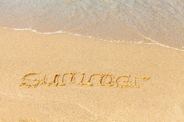 Text on a sunny beach. The word Summer is handwritten in sand, washed away by a sea wave. Vacation concept on a sandy beach. Copy space.