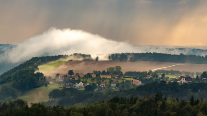 View from the Gamrig to the village Weißig in the saxon switzerland with rising fog and rain in the sunset