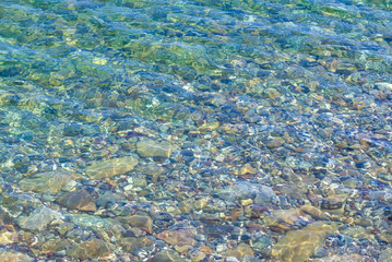 Transparent sea water washes underwater pebbles. The finely stony bottom is visible through the crystal clear sea surface of the water.