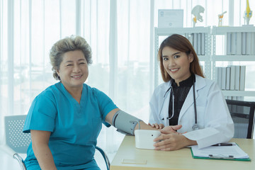  a young beautiful asian doctor is using blood pressure for senior patient with smiling face.