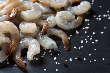 large raw peeled shrimp with coarse sea salt on black background