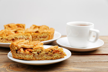 Homemade pie with apples and cinnamon and a cup of tea on white wooden table. Shallow focus.