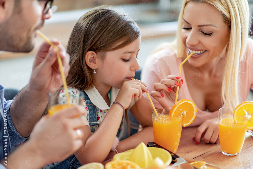 Wall mural Cheerful young family drinking orange juice