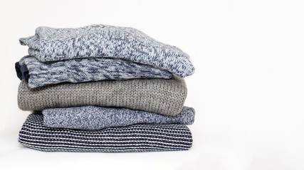 Stack of folded woolen knitwear on white background. Season of warm knitted clothes: sweaters, jumpers, cardigans. Autumn-winter wardrobe concept. Winter is coming. Closeup. Copy space