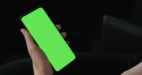 Young woman sitting on a chair near window and using smartphone with green screen