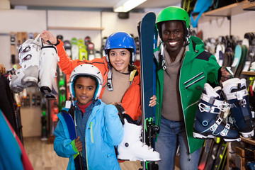 Smiling young African man and European woman with preteen son standing with purchased ski equipment...