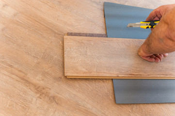 Craftsman laying laminate flooring using a substrate is trimmed with a clerical knife. Repair in the apartment.