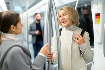 Two women passengers talking in subway car on way to work