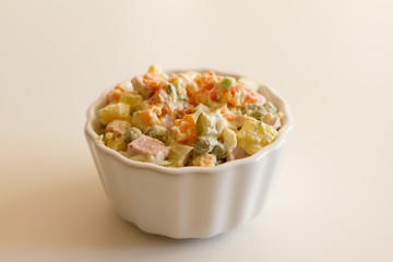 Olivier in a white plate on a pale pink background. the winter salad.ingredients: cucumber, sausage, meat, mayonnaise, sour cream, potatoes, peas, egg. space for your text.