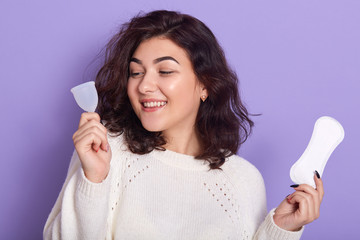 Woman holding menstrual cup and sanitary pad in hands. Feminine hygiene alternative product instead...
