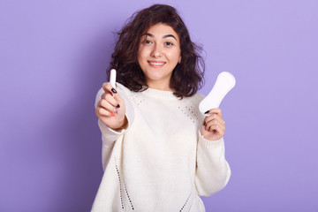 Fototapeta na wymiar Portrait of cheerful attractive young lady holding tampon and sanitary napkin, making choices during menstruation, making preferance to tampon, looking directly at camera. Menstruation concept.