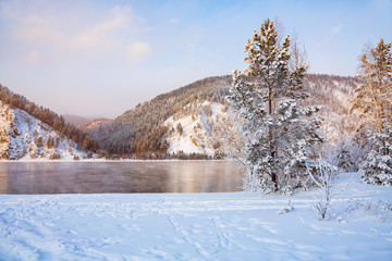 Beautiful snowy winter landscape with river and mountains. Frosty clear sunny day with blue sky.