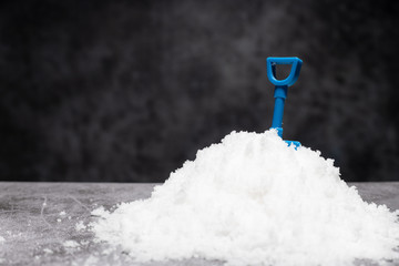 Blue toy shovel on snow with copy space on black background.