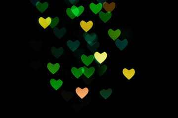 Multicolored hearts bokeh of green and yellow colores on black background. Texture for holidays