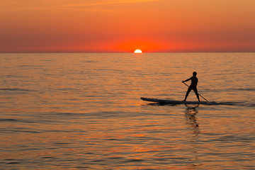paddle standing board, beach leisure activity, beautiful silhouette of man at sunset. Romantic colorful sunset at the sea. Sun go down