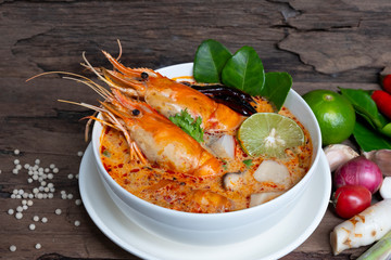 Tom Yum Goong or Shrimp soup spicy sour Soup Traditional food in Thailand contains chili, lime,lemongrass, lime leaf, along with cooked rice in a white dish on the old wood background from top view.