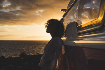 Travel and independence concept with woman in silouette and old vintage camper van - coloured dawn sunset in background with ocean and horizon - Powered by Adobe