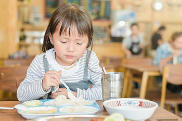 Little asian child girl with unhappy face while having lunch on table in restaurant,picky eater...
