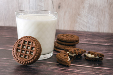 sandwich cookies and a glass of milk on a wooden table.