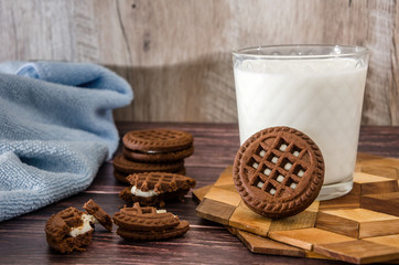 sandwich cookies and a glass of milk on a wooden table.