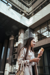 the girl on the street bit off a pie and looks at him with a smile of amazement against the background of glass buildings