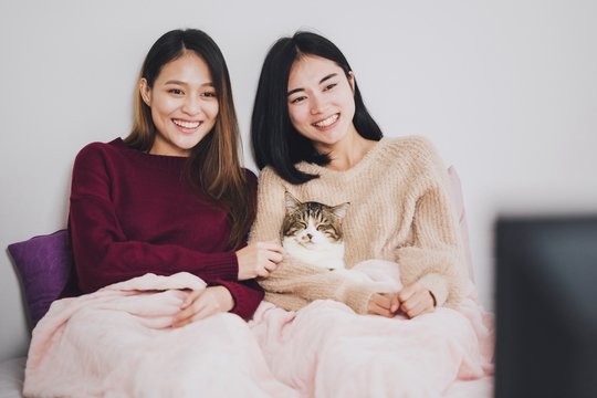 Young beautiful Asian women lesbian couple lover watching television on the bed with the cat together in bed room at home with smiling face.Concept of LGBT sexuality with happy lifestyle together.