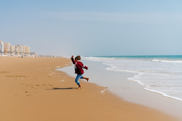 the figure of a woman in warm clothes is jumping along a deserted beach, the ocean is rolling its waves