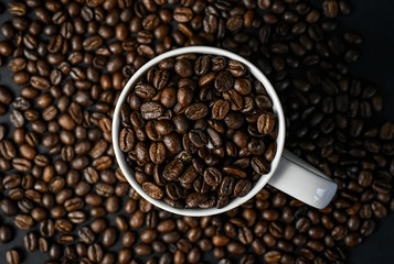 Coffee beans in a white coffee mug surrounded by coffee beans